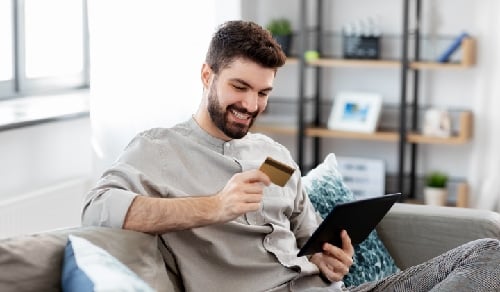 A smiling man holding his credit card and his Ipad on the other hand.